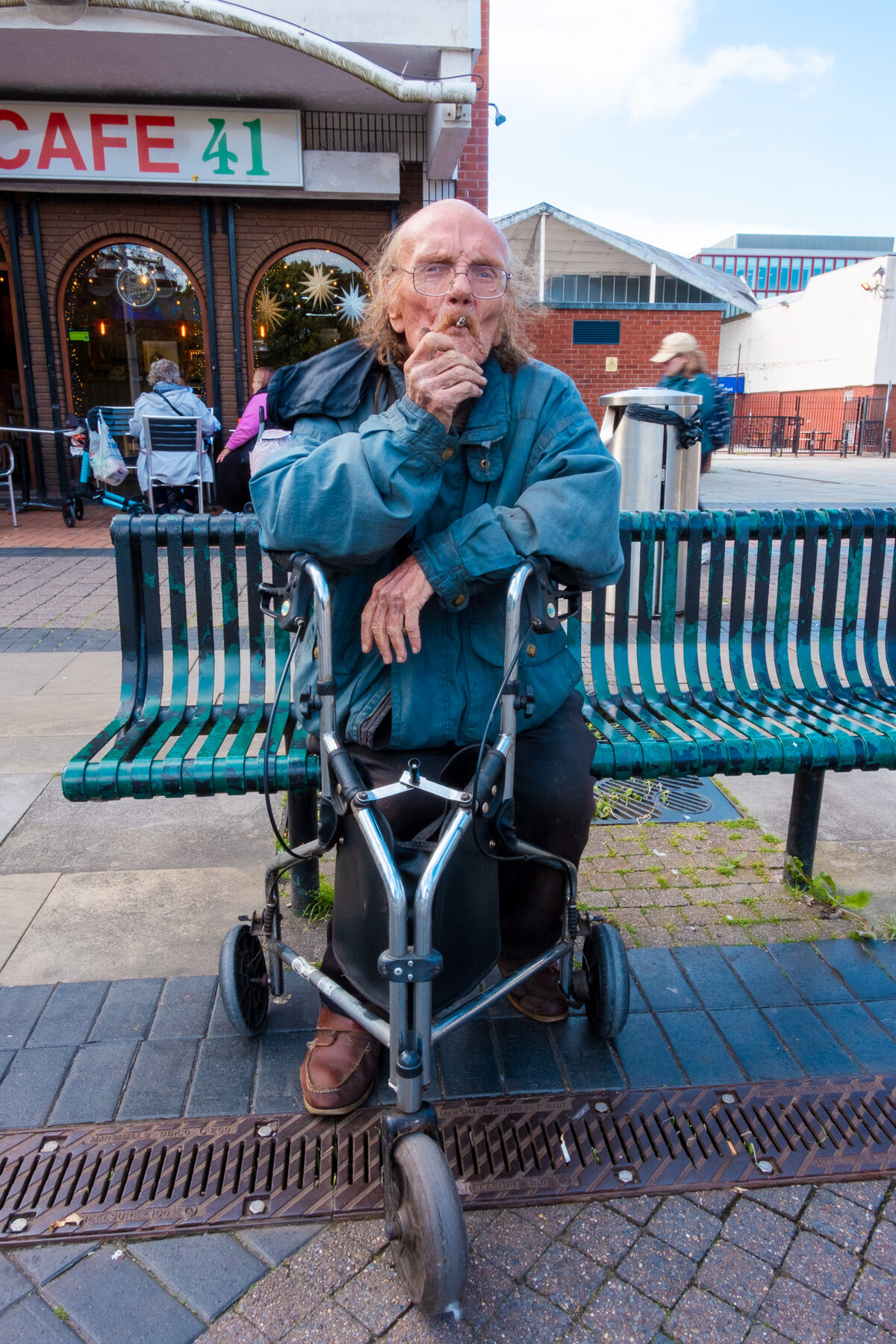 An elderly man with a walking frame seated outside Cafe 41