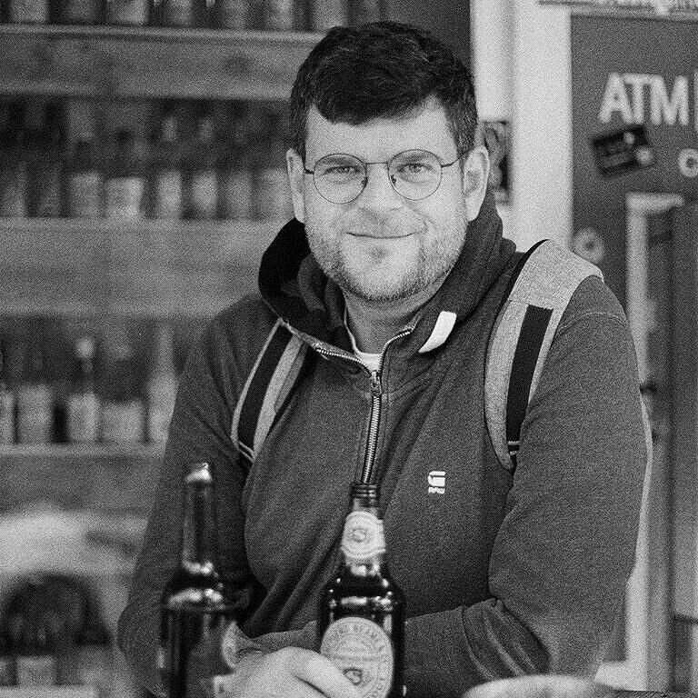 Rory Wilmer at a bar with two bottles of beer, black and white