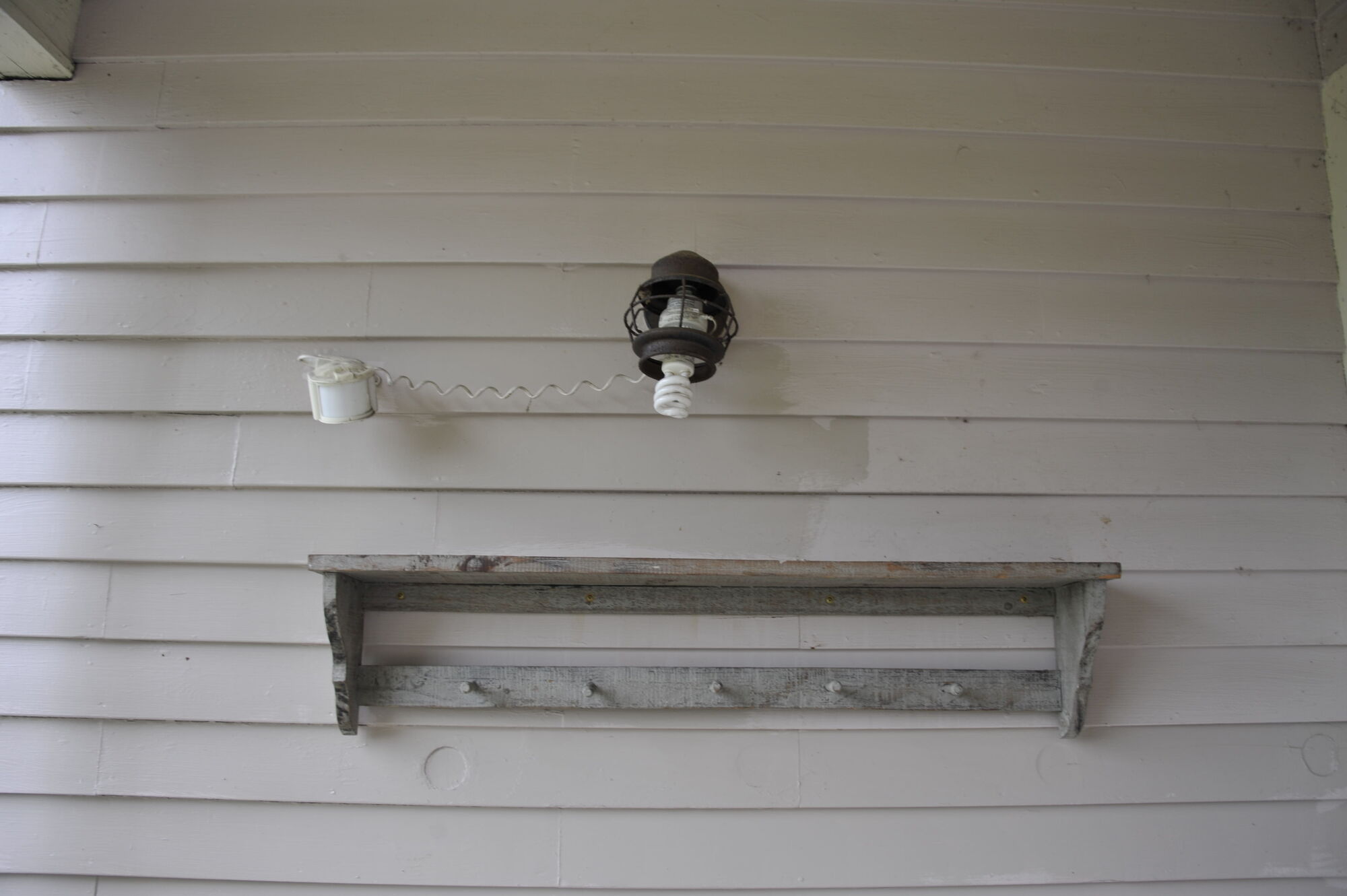 A porch lamp and old wooden shelf on the white boarded wall