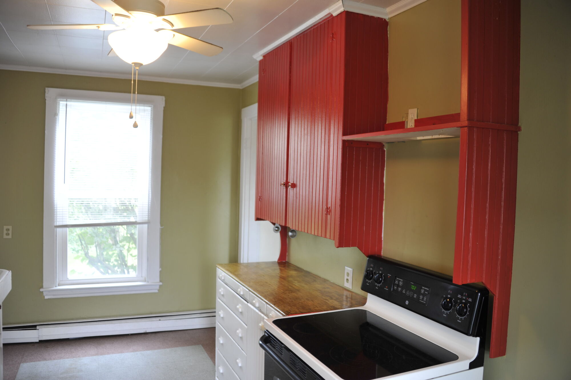 The kitchen with red beadboard cabinets, stove and ceiling fan